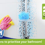 7 Great reasons to prioritise cleaning the bathroom Person wearing pink glove cleaning a bathroom wall with a microfiber cloth.